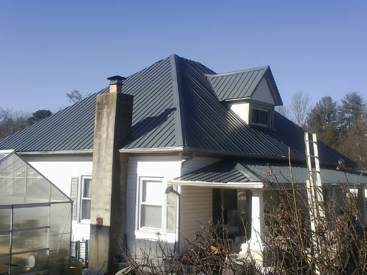 Dark blue standing seam metal roof on a white farmhouse with dormer — Slate & Tile Roof Repair by Roofing Brothers in Calverton