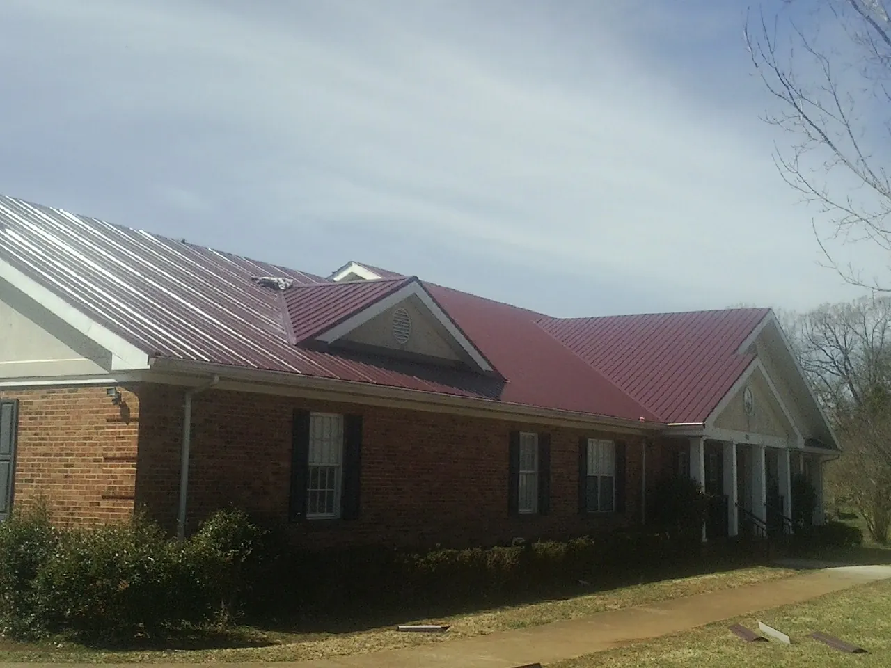 Red metal roof with gabled entries on a long brick building, from a Hail Damage Roof Repair job in Calverton