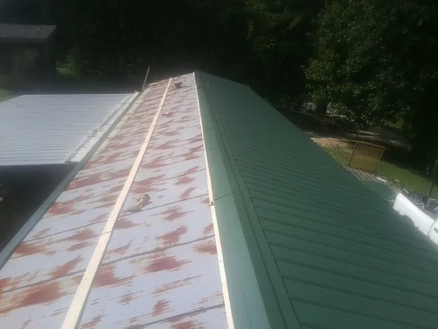 Old rusted panels beside newly installed green metal roofing — Wind Damage Roof Repair by Roofing Brothers in Calverton