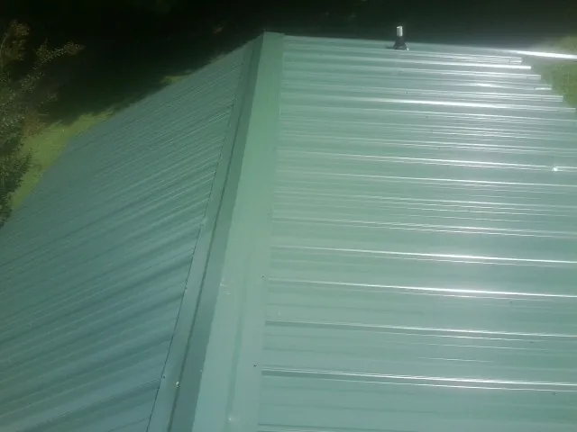 New green metal panels meeting at the ridge of a roof — Flat Roof Repair work by our crew in Calverton