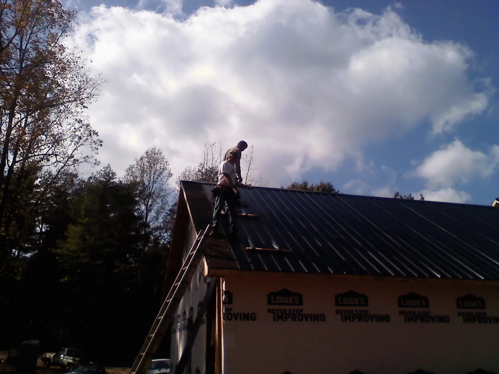 Roofer fastening dark metal panels high against a cloudy sky, from a Roof Inspection job in Calverton