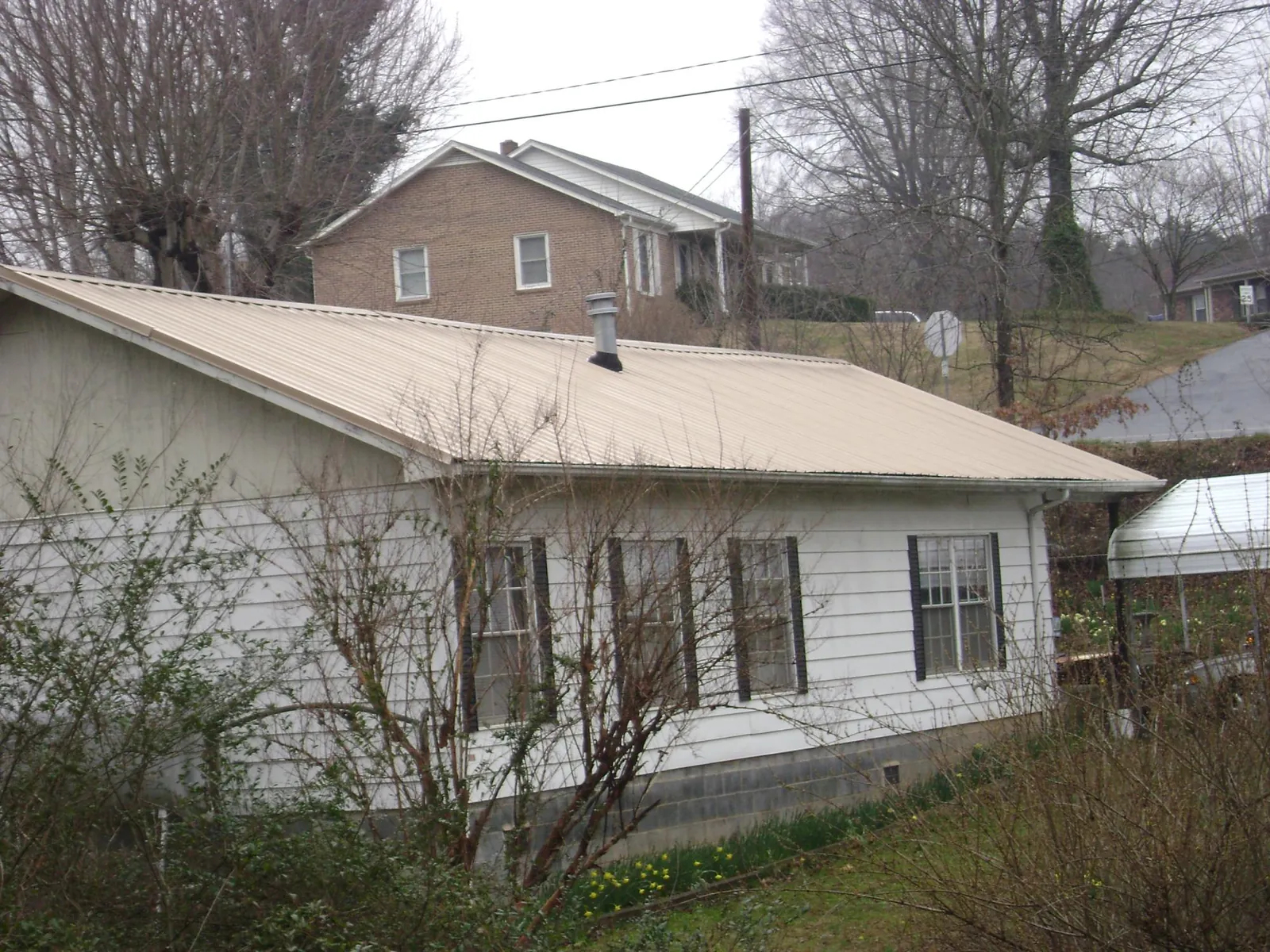 Tan metal roof on a white sided house set into a hillside in Calverton