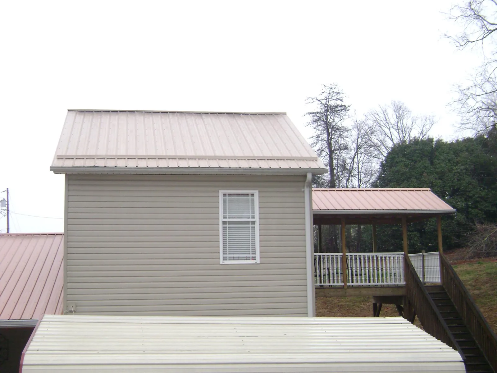 Tan metal roofs on a two story addition and attached porch, from a Roof Replacement job in Calverton